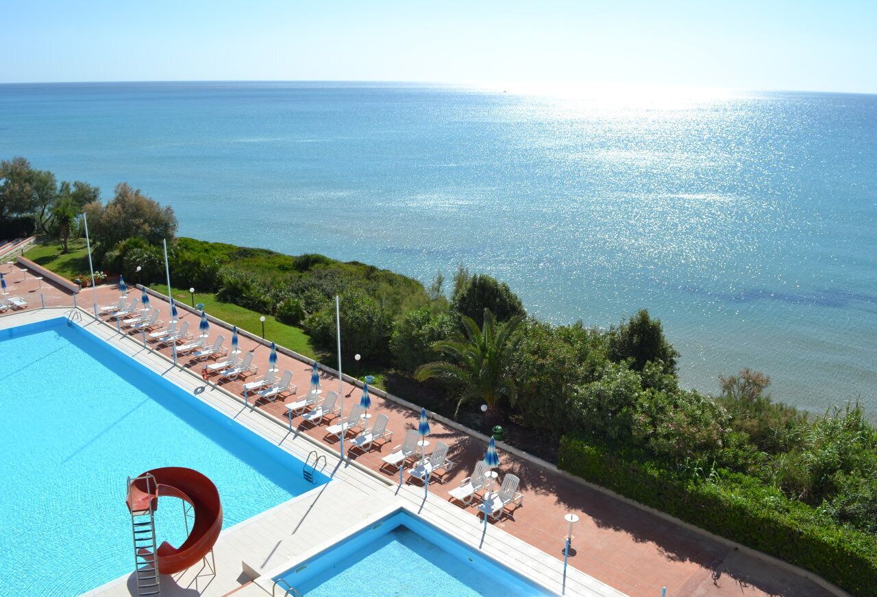 En pool med en vattenrutschkana, solstolar och utsikt över havet.