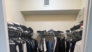 A walk-in closet with hanging clothes, a laundry basket, and a door. - Spacious 3-bedroom condo in charming Royal Palm Beach with AC (Royal Palm Beach)
