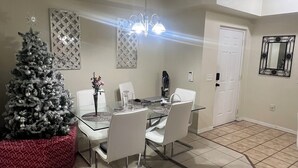 A dining area with a glass table, white chairs, a Christmas tree, and a chandelier. - Spacious 3-bedroom condo in charming Royal Palm Beach with AC (Royal Palm Beach)