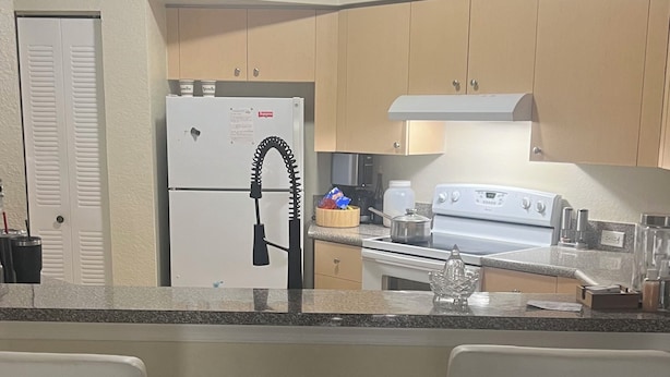 A kitchen with a refrigerator, stove, and two bar stools. - Spacious 3-bedroom condo in charming Royal Palm Beach with AC (Royal Palm Beach)