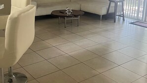 A living room with a white sofa, a coffee table, a ceiling fan, and a large window with blinds. - Spacious 3-bedroom condo in charming Royal Palm Beach with AC (Royal Palm Beach)