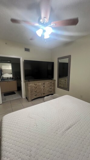 Un dormitorio con cama, cómoda, televisor y ventilador de techo.