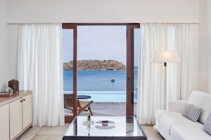 Una sala de estar moderna con una mesa de vidrio, sofá blanco y vistas a un paisaje costero a través de amplios ventanales.