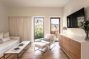 Una sala de estar moderna con un sofá, una mesa de centro, un sillón, un televisor y vistas a un paisaje montañoso.