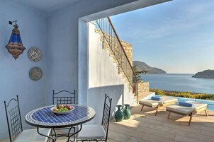 A balcony with a table, chairs, and a view of the sea.