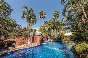 A swimming pool surrounded by palm trees and a rocky landscape. - Travelodge Resort Darwin (Darwin)