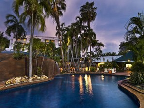 A swimming pool surrounded by palm trees and a building with multiple balconies. - Travelodge Resort Darwin (Darwin)