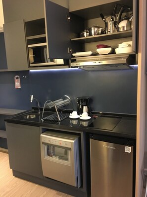 A compact kitchen with a built-in oven, a coffee machine, and a sink with a dish rack.