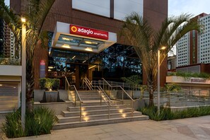 The exterior of Adagio Aparthotel with a modern design, featuring a staircase leading to the entrance, surrounded by palm trees and a glass facade.