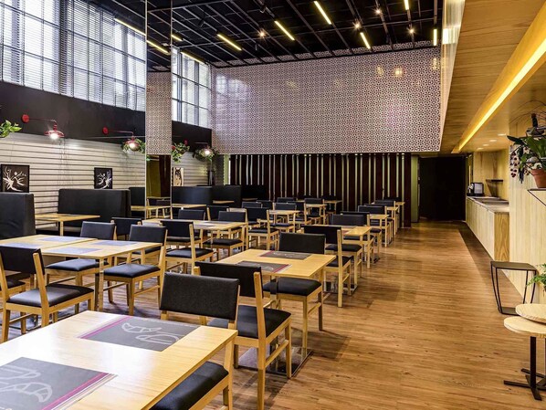 A modern restaurant with wooden tables and chairs, a patterned wall, and a kitchen area.