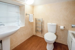 Ein Badezimmer mit Waschbecken, Toilette, Handtuchhalter und einem Fenster mit Jalousien.