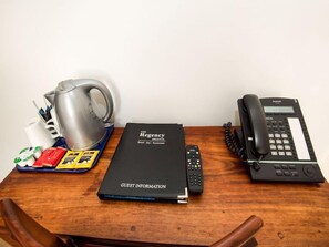 Ein Holztisch mit einem schwarzen Gästeinformationsbuch, einem silbernen Wasserkocher, einer Fernbedienung, einem schwarzen Telefon und einer Ablage mit verschiedenen Gegenständen.