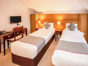 A hotel room with two single beds, a desk, a chair, a television, and a wooden headboard. - The Regency, Clifton Bristol (Bristol)