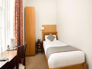 Ein Hotelzimmer mit Bett, Nachttisch, Lampe, Stuhl, Schreibtisch und Kleiderschrank.
