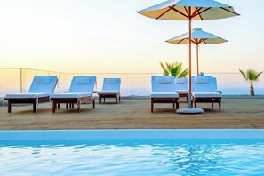 A poolside area with lounge chairs and umbrellas. - Villaggio Boutique Hotel Hersonissos - Adults Only (Hersonissos)