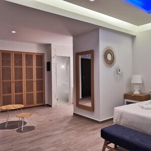 A modern hotel room with a bed, a bedside table with a lamp, a large mirror, and a wardrobe. - Villaggio Boutique Hotel Hersonissos - Adults Only (Hersonissos)