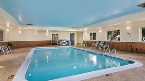 Una piscina interior con agua cristalina, rodeada de sillones de descanso y un muro de madera.