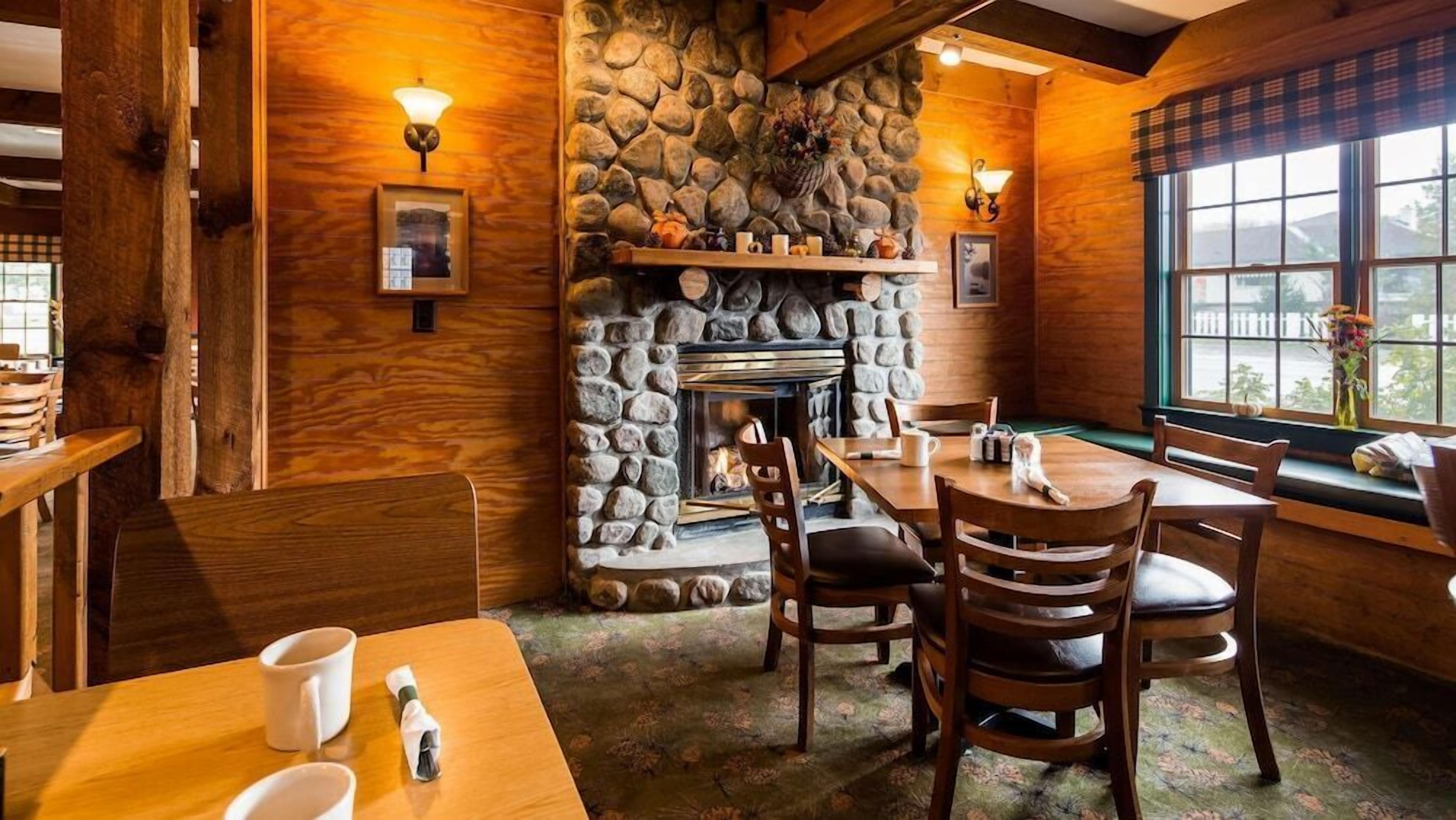 A cozy interior with a stone fireplace, wooden walls, and a dining area with chairs and tables.