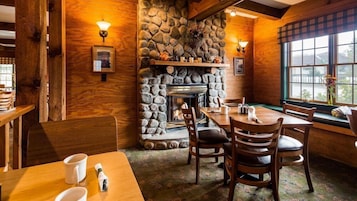 Un interior acogedor con chimenea de piedra, paredes de madera y un comedor con sillas y mesas.