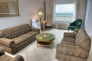 Un salón con sofá, sillón y una mesita con lámpara.
