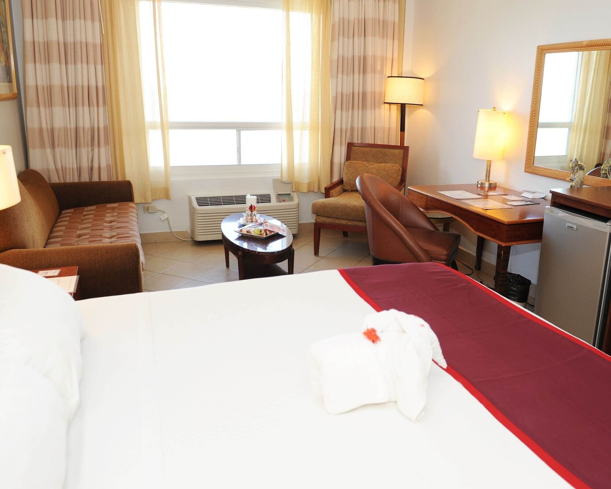 Une chambre d’hôtel avec un lit, un bureau, une chaise, une table et une fenêtre avec des rideaux.