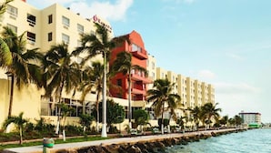 A hotel with a red and beige facade, palm trees, and a waterfront view. - Ramada by Wyndham Princess Belize City (Belize City)