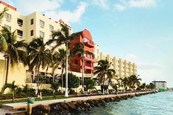 A hotel with a red and beige facade, palm trees, and a waterfront view. - Ramada by Wyndham Princess Belize City (Belize City)