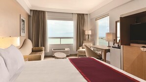 A hotel room with a bed, a desk, a chair, a TV, and a view of the sea. - Ramada by Wyndham Princess Belize City (Belize City)