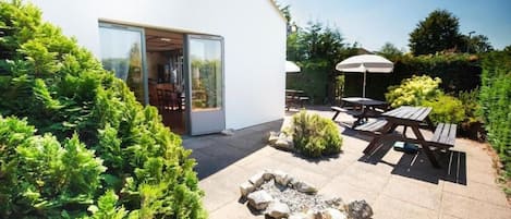 Un patio moderno al aire libre con un brasero, mobiliario de madera y un ventanal de vidrio que da a un espacio interior.