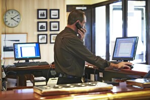 A man working at a desk with two computer monitors, a clock, and framed pictures on the wall. - Campanile Washington Newcastle-upon-tyne (Washington)