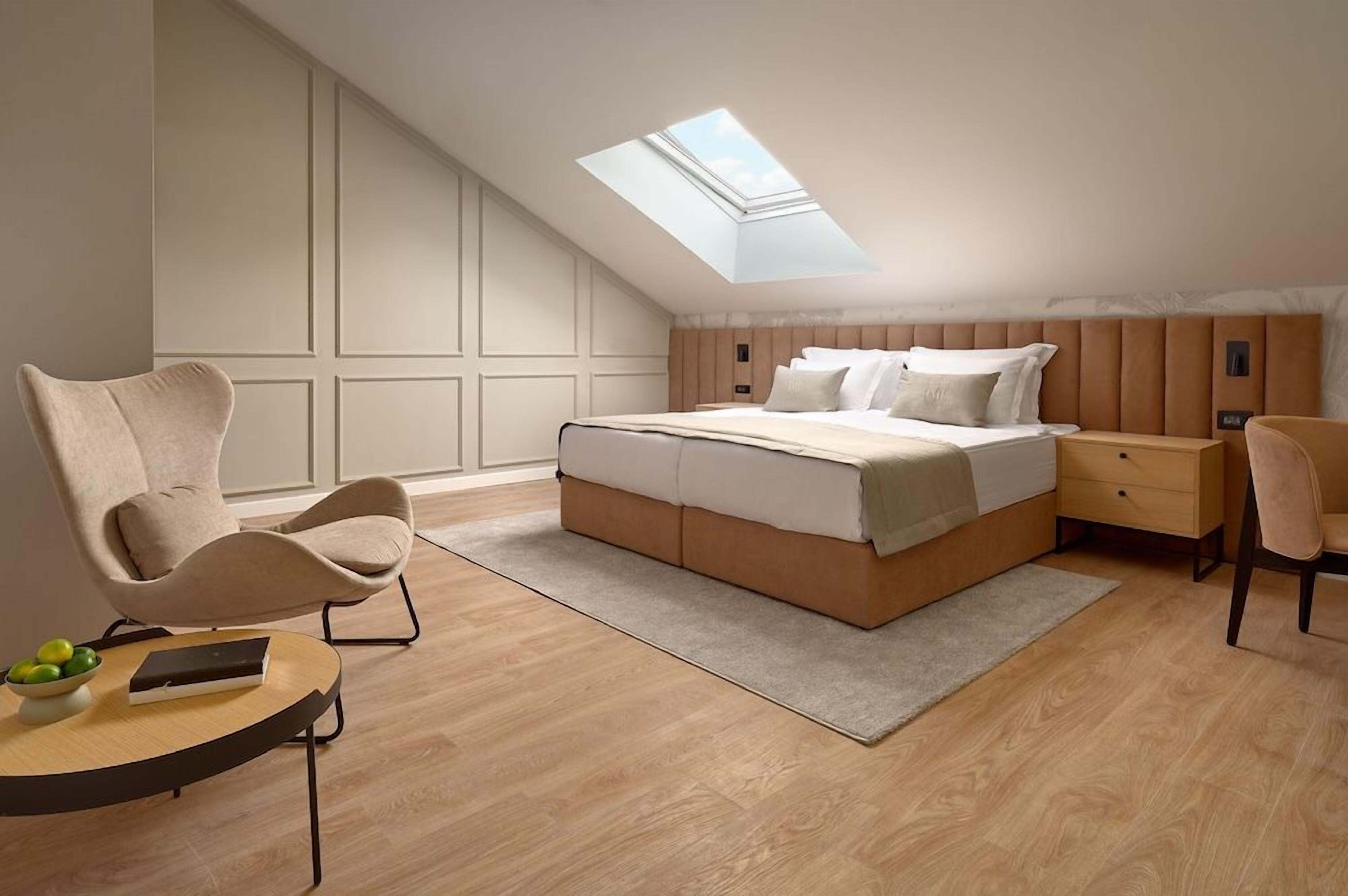 Un dormitorio con tragaluz, una cama, una mesita de noche, una silla y una pequeña mesa con un cuenco de fruta.