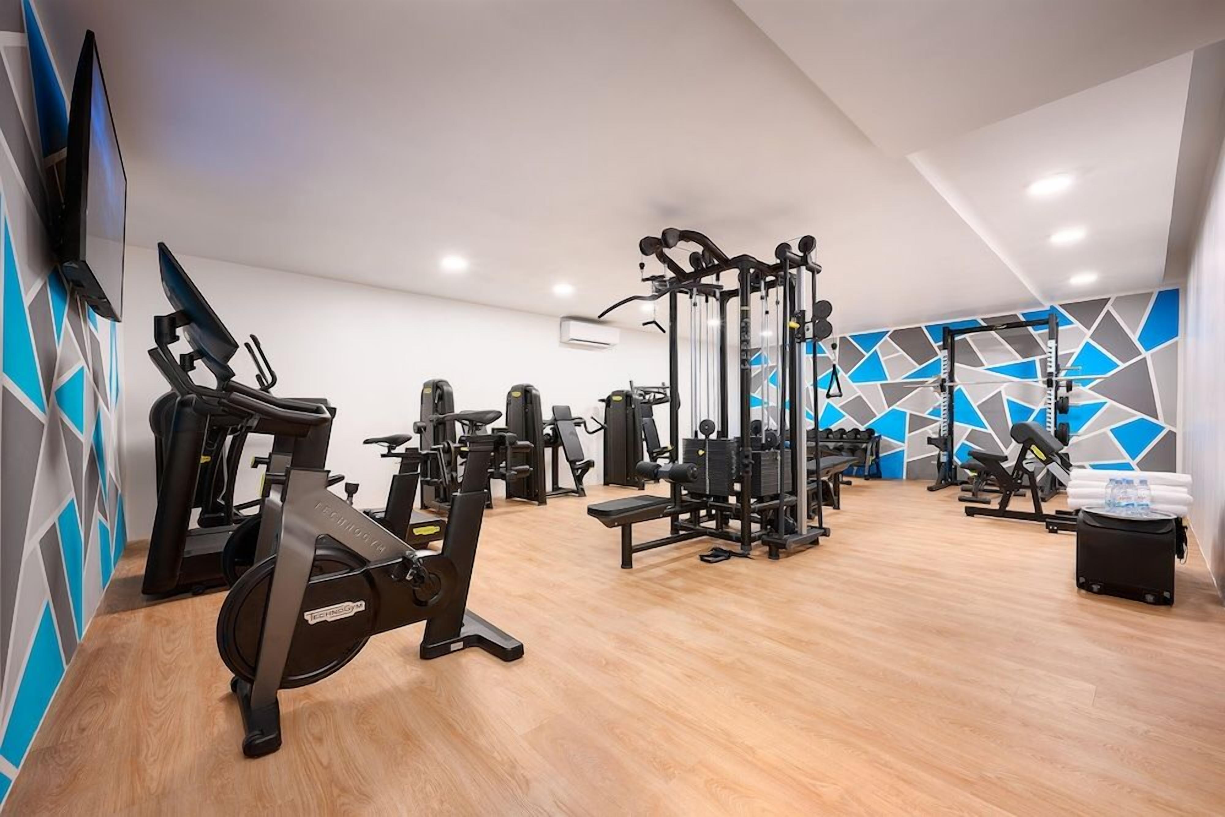 Un gimnasio con equipo de ejercicio, un televisor instalado en la pared y un revestimiento mural con diseño geométrico.