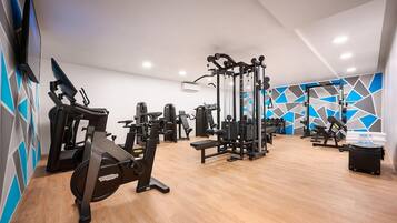 Un gimnasio con equipo de ejercicio, un televisor instalado en la pared y un revestimiento mural con diseño geométrico.