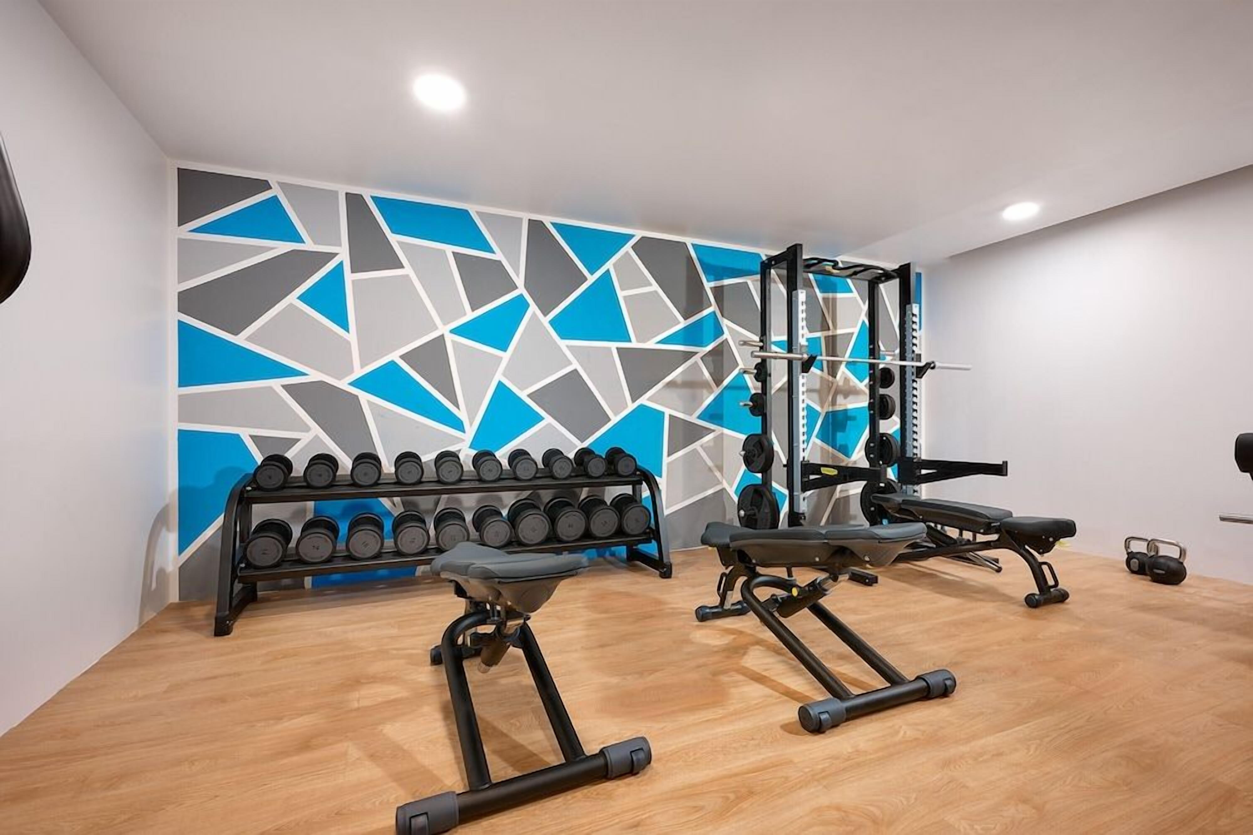 A gym with exercise equipment, a rack of dumbbells, and a geometric wall design.