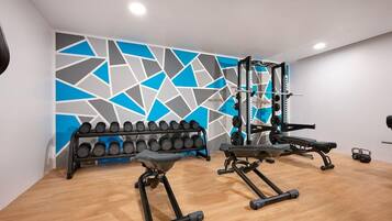 A gym with exercise equipment, a rack of dumbbells, and a geometric wall design.