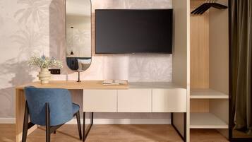 A modern room with a flat-screen TV mounted on the wall, a desk with a chair, a mirror, and a wardrobe with a hanging rack.