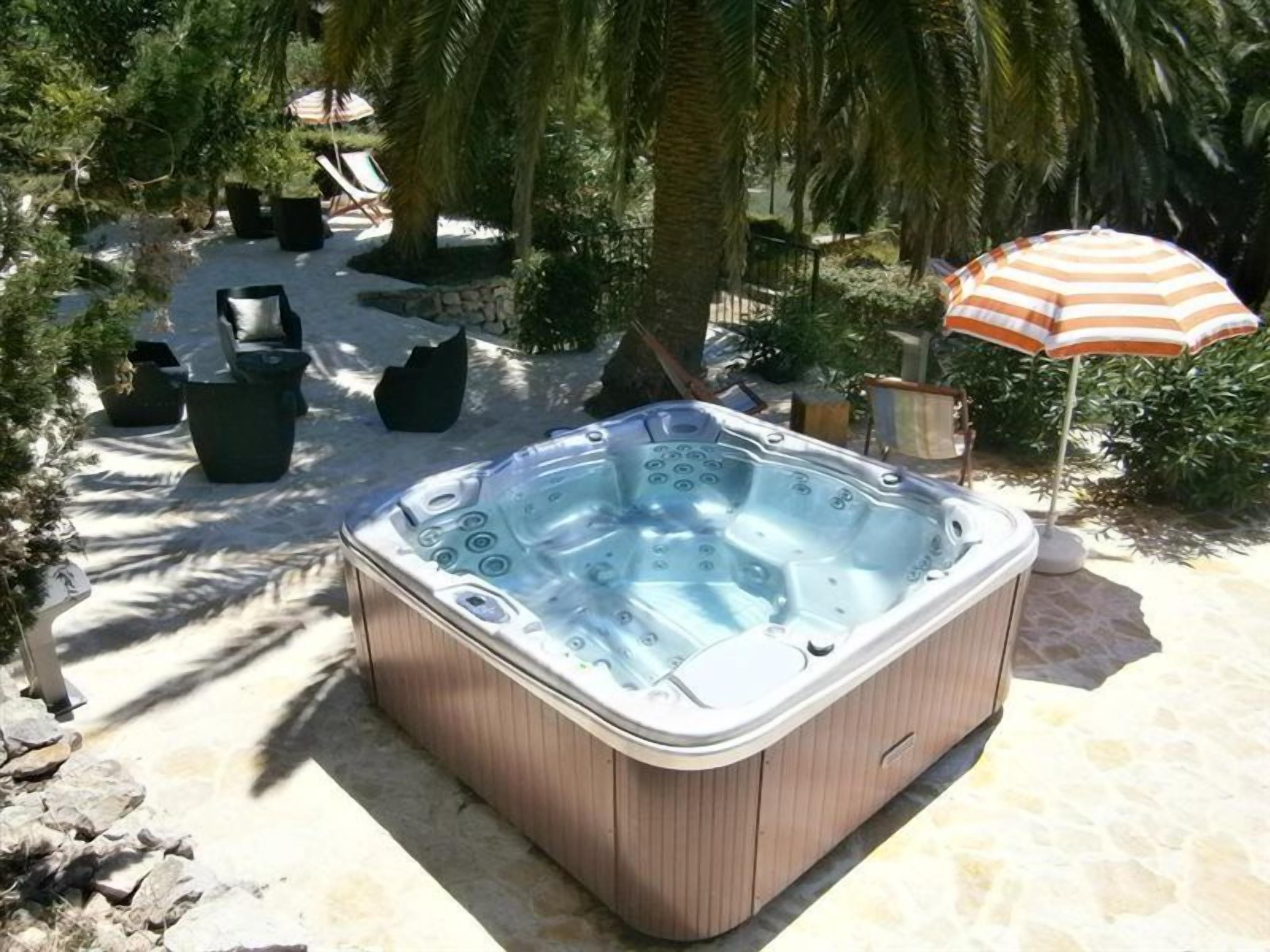 Un jacuzzi en un jardín con sillones de descanso y una sombrilla.