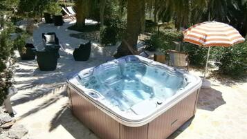 Un jacuzzi en un jardín con sillones de descanso y una sombrilla.