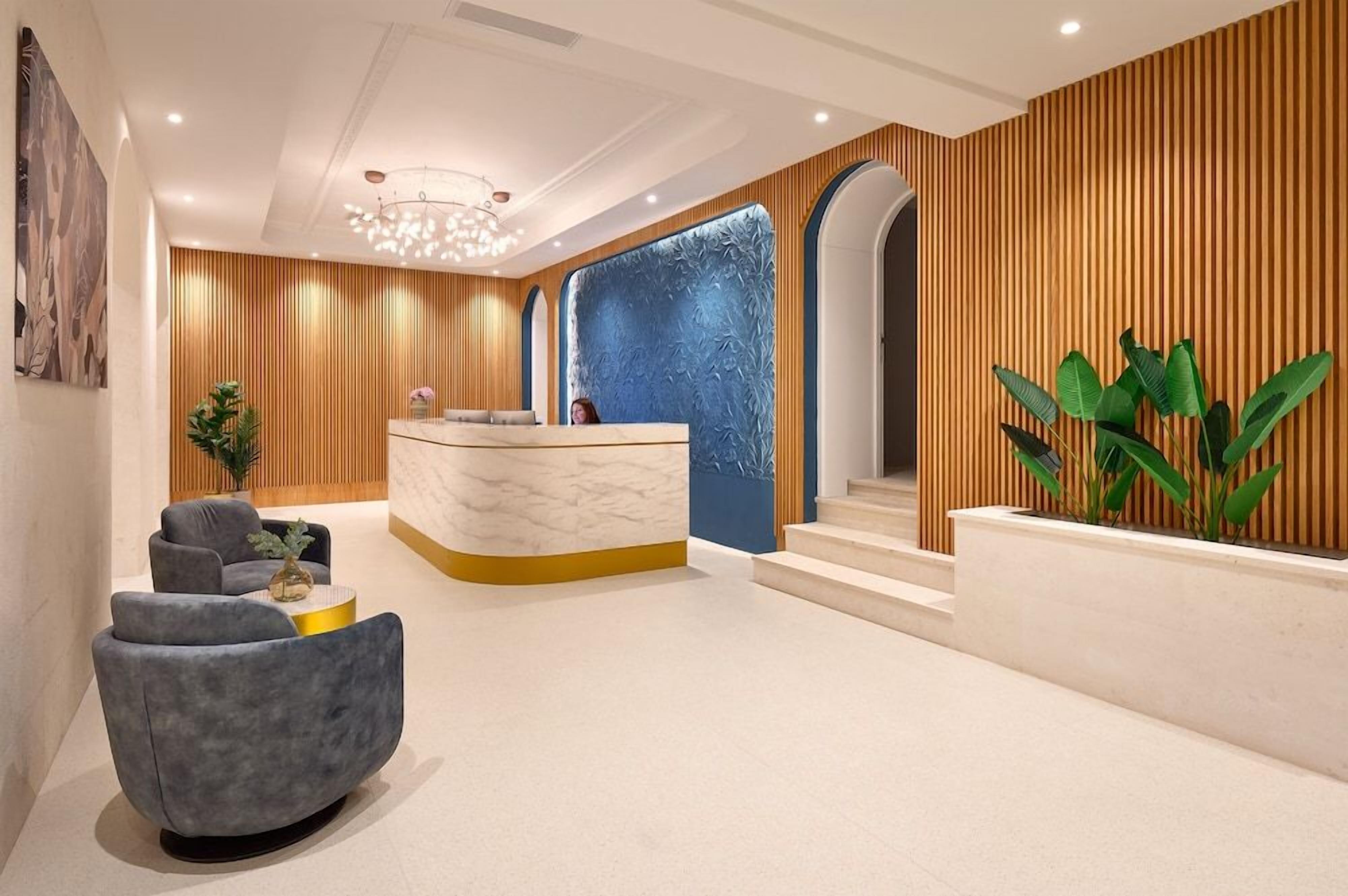 Un área de recepción moderna con un mostrador de mármol, asientos tapizados en gris y una planta grande.