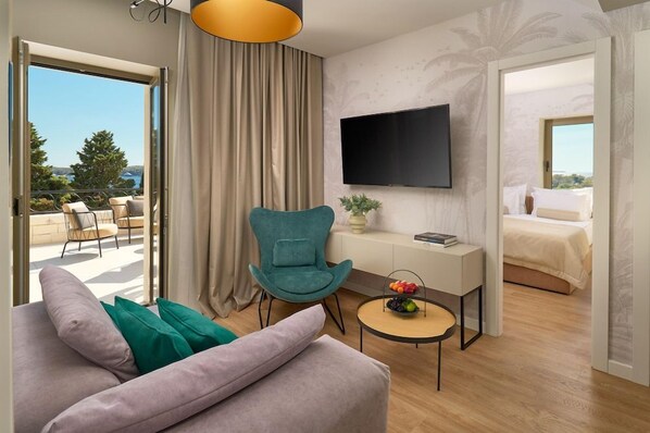 A modern hotel room with a balcony, a teal armchair, a small round table with a fruit bowl, a flat-screen TV mounted on the wall, and a bed with a white duvet. - Hotel Moeesy Blue Green Oasis Ex Croatia Hotel Hvar (Hvar)