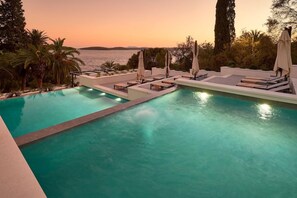 A pool with lounge chairs and umbrellas, surrounded by greenery and overlooking a body of water. - Hotel Moeesy Blue Green Oasis Ex Croatia Hotel Hvar (Hvar)