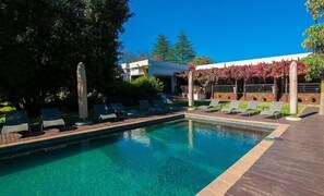 Una piscina con sillas de descanso y un pérgola con follaje rojo.