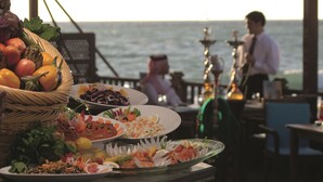 A dining table with various dishes and a basket of fruits, overlooking the sea. - Movenpick Resort Al Nawras Jeddah (Jeddah)