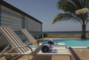 Zona de descanso junto a la piscina con tumbonas, toallas y vistas al océano.