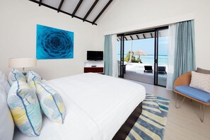 A hotel room with a bed, a TV, a view of the beach, and a balcony with a chair. - NH Collection Maldives Havodda Resort (Havodda)