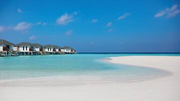 Overwater bungalows with a clear view of the turquoise sea and white sand beach.