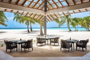 A beachside dining area with a glass ceiling, palm trees, and a view of the ocean. - NH Collection Maldives Havodda Resort (Havodda)