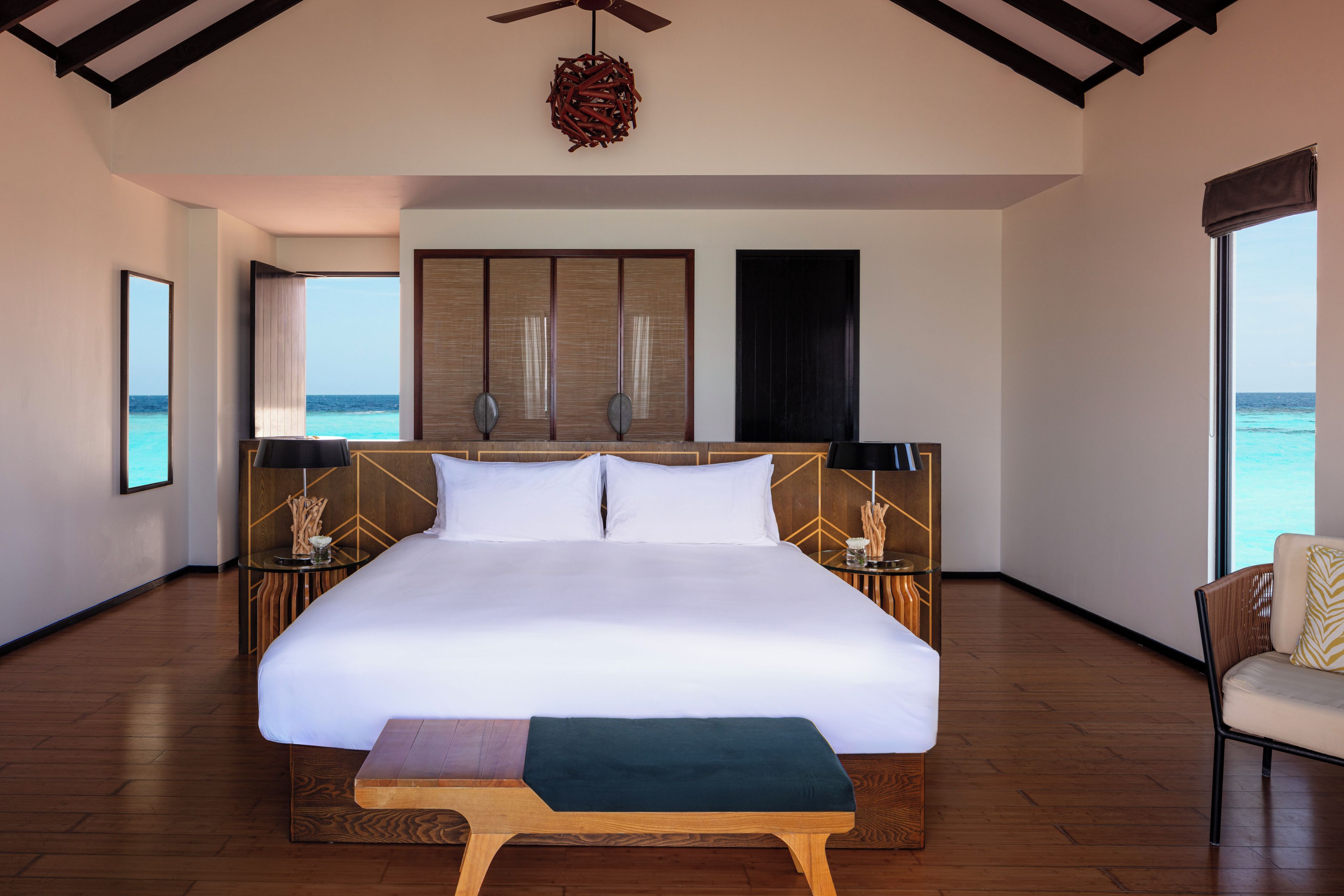 A spacious bedroom with a large bed, a wooden floor, a ceiling fan, and a view of the ocean.