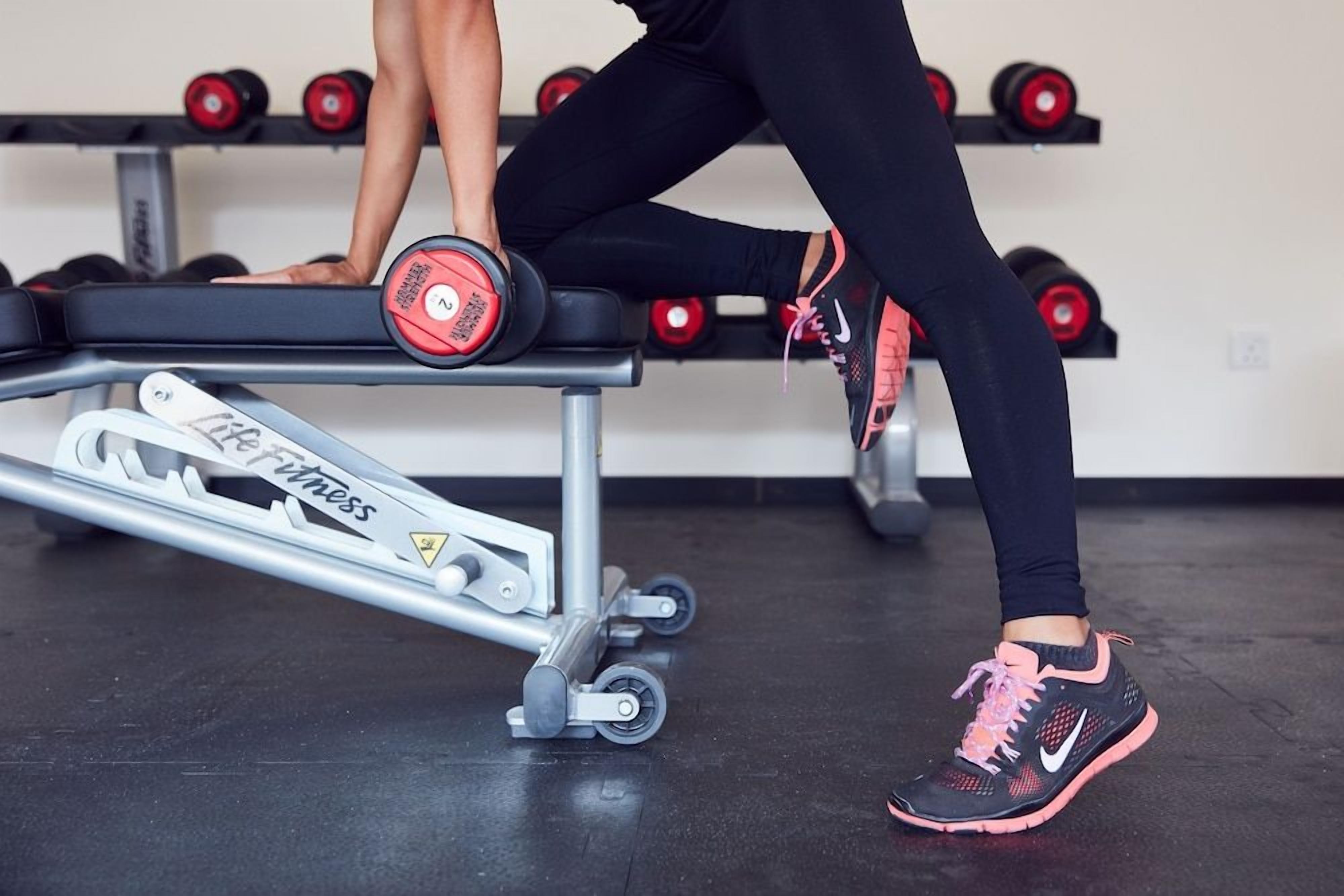 A gym setting with a bench, dumbbells, and a weightlifting machine.