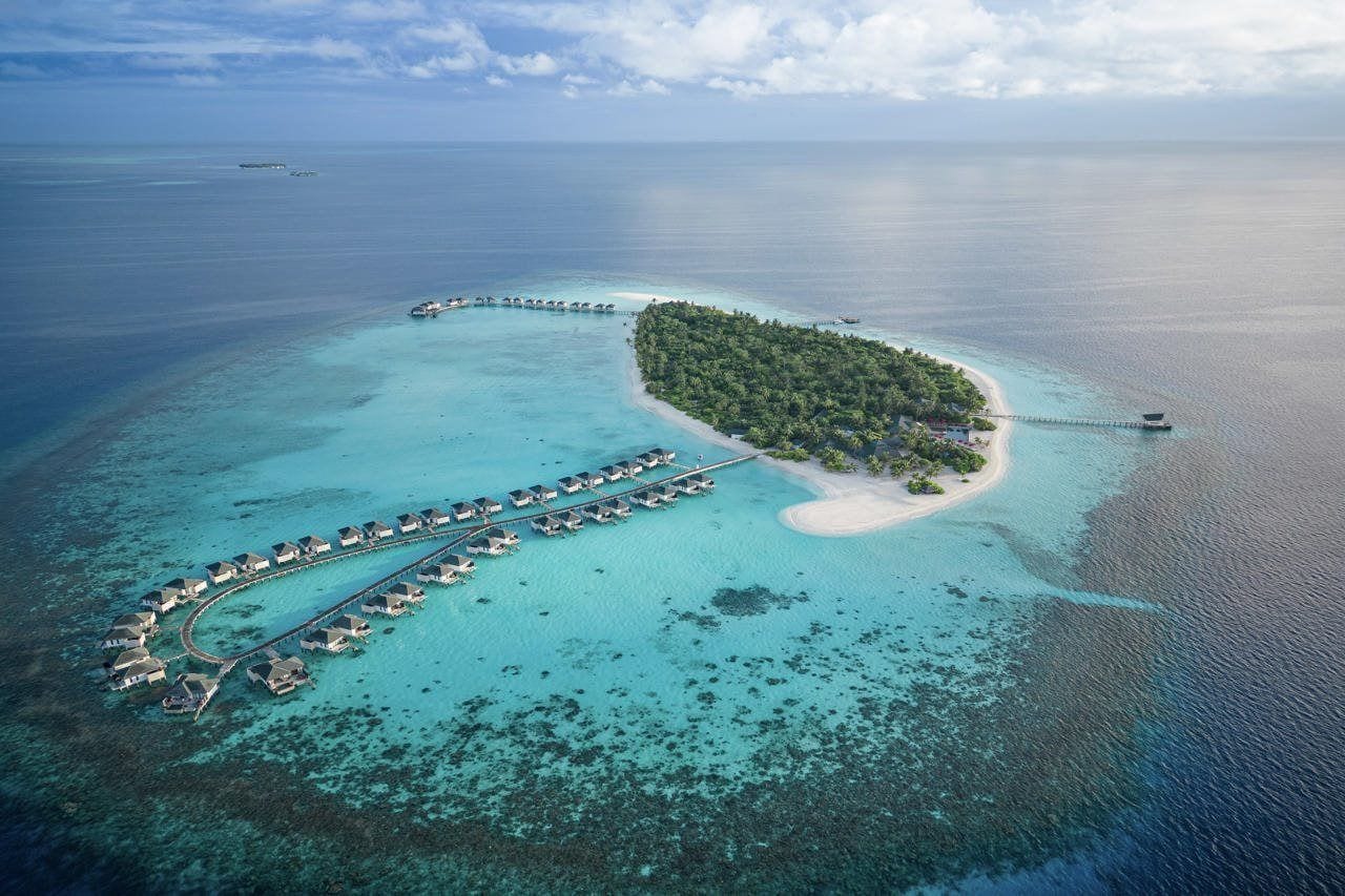 An aerial view of a tropical island with overwater bungalows connected by a dock.